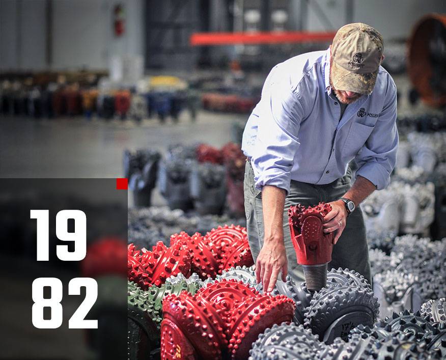 Worker inspecting tricone drill bits inside KS Bit warehouse.